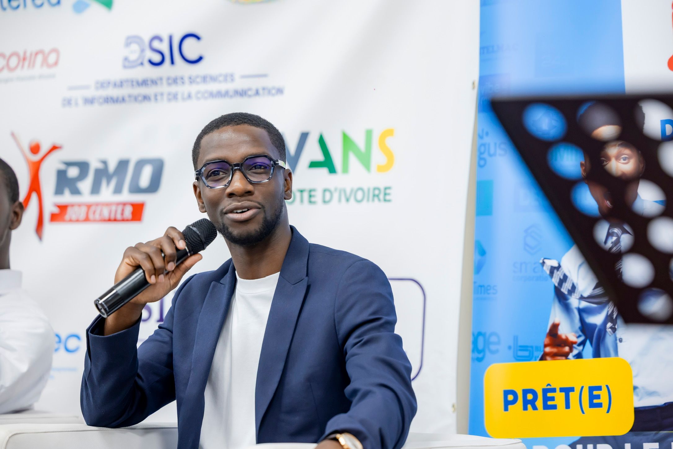 Axel Loupeda, lunettes et blazer bleu, parle au micro lors de la table ronde de la Journée de l'Emploi à Abidjan