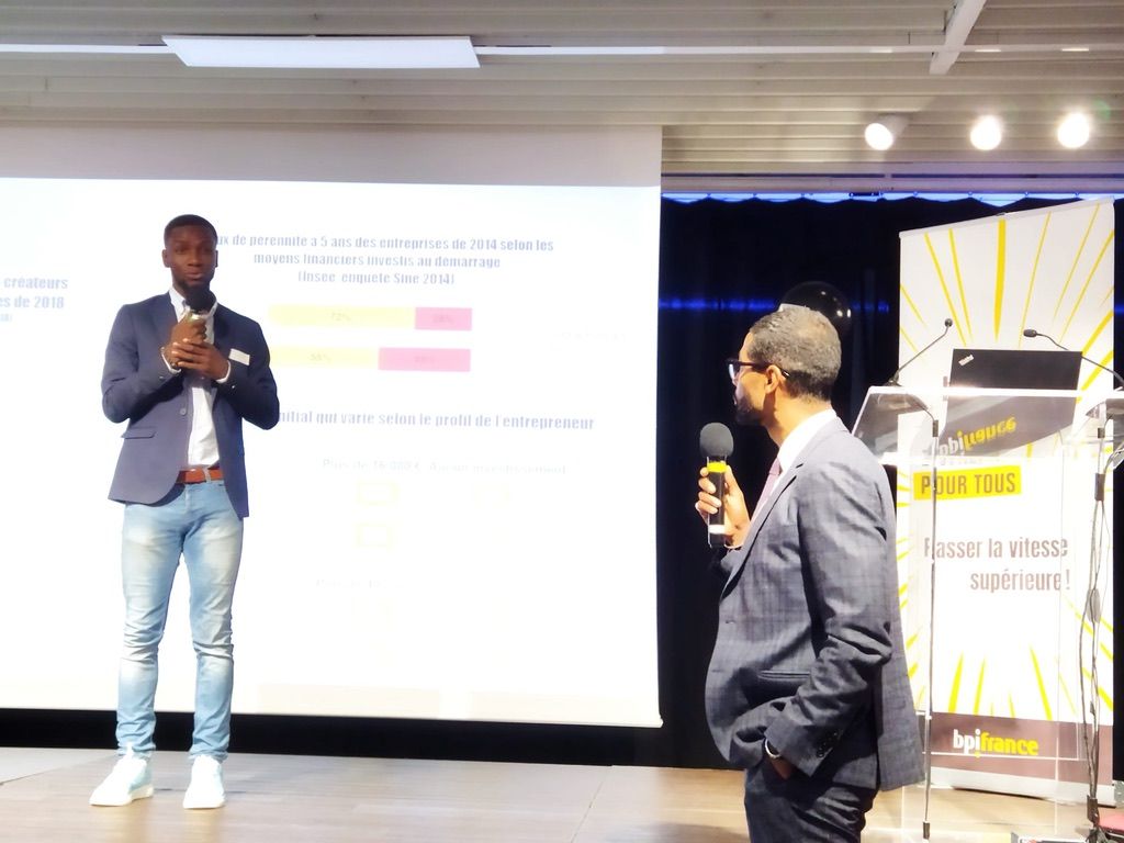 Axel Loupeda, micro en main, présente devant un écran de projection, aux côtés d'un modérateur